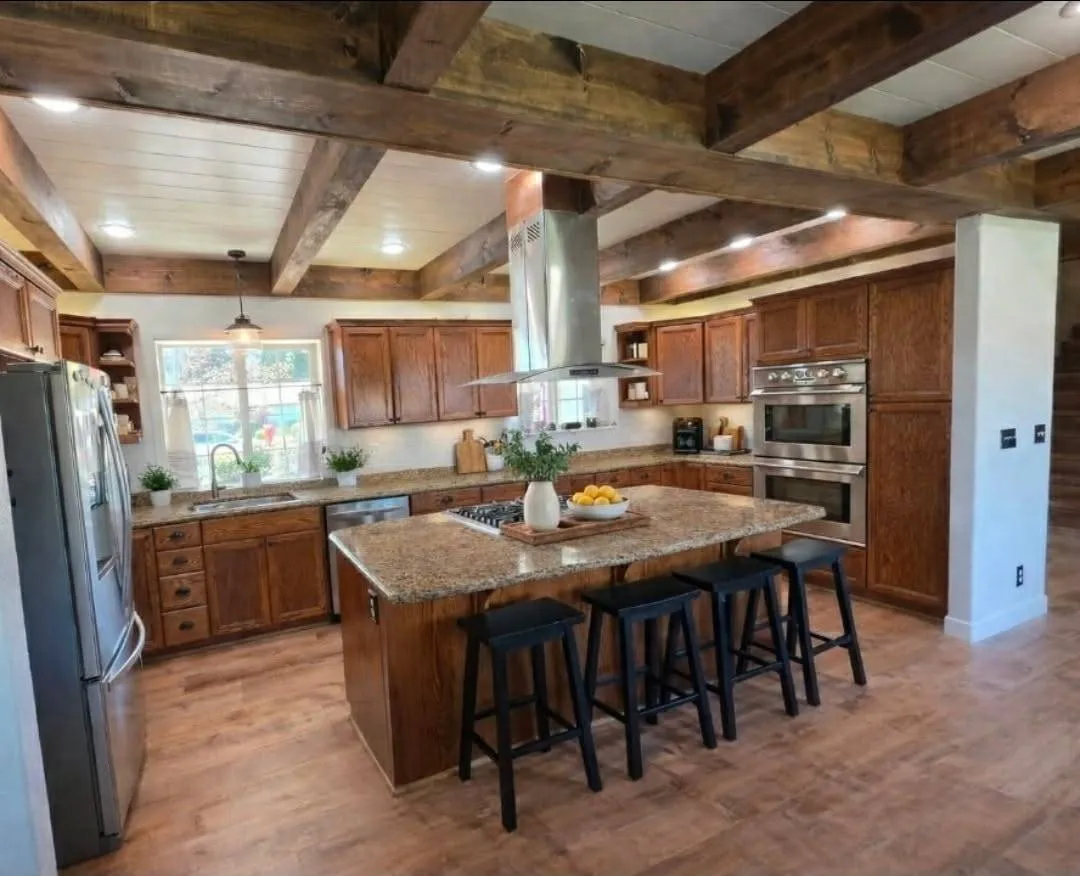 Open kitchen with exposed wood beam ceiling, island, and stainless appliances