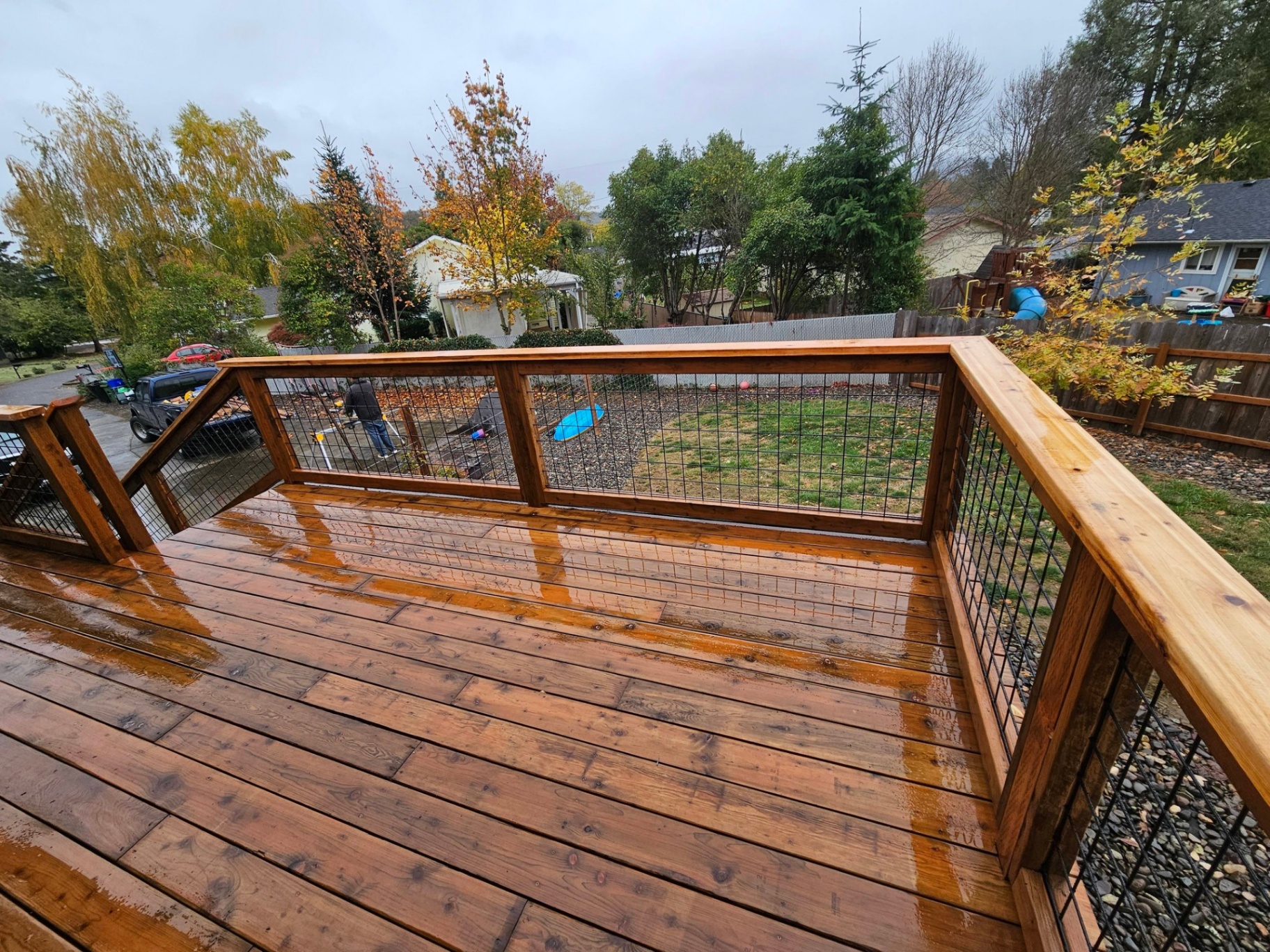 Freshly sealed cedar deck with hog-wire railings on a rainy afternoon